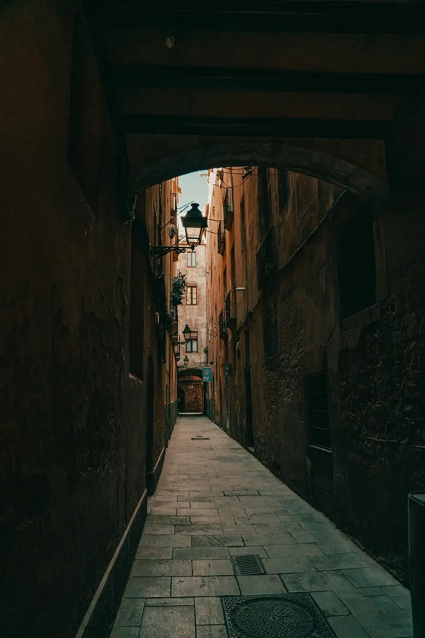 A narrow stone alley in El Born seen through a dark archway, with a wall lamp