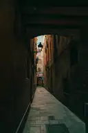 A narrow stone alley in El Born seen through a dark archway, with a wall lamp