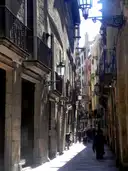 A sunny narrow street in Barcelona's Gothic Quarter lined with iron balconies and lamps