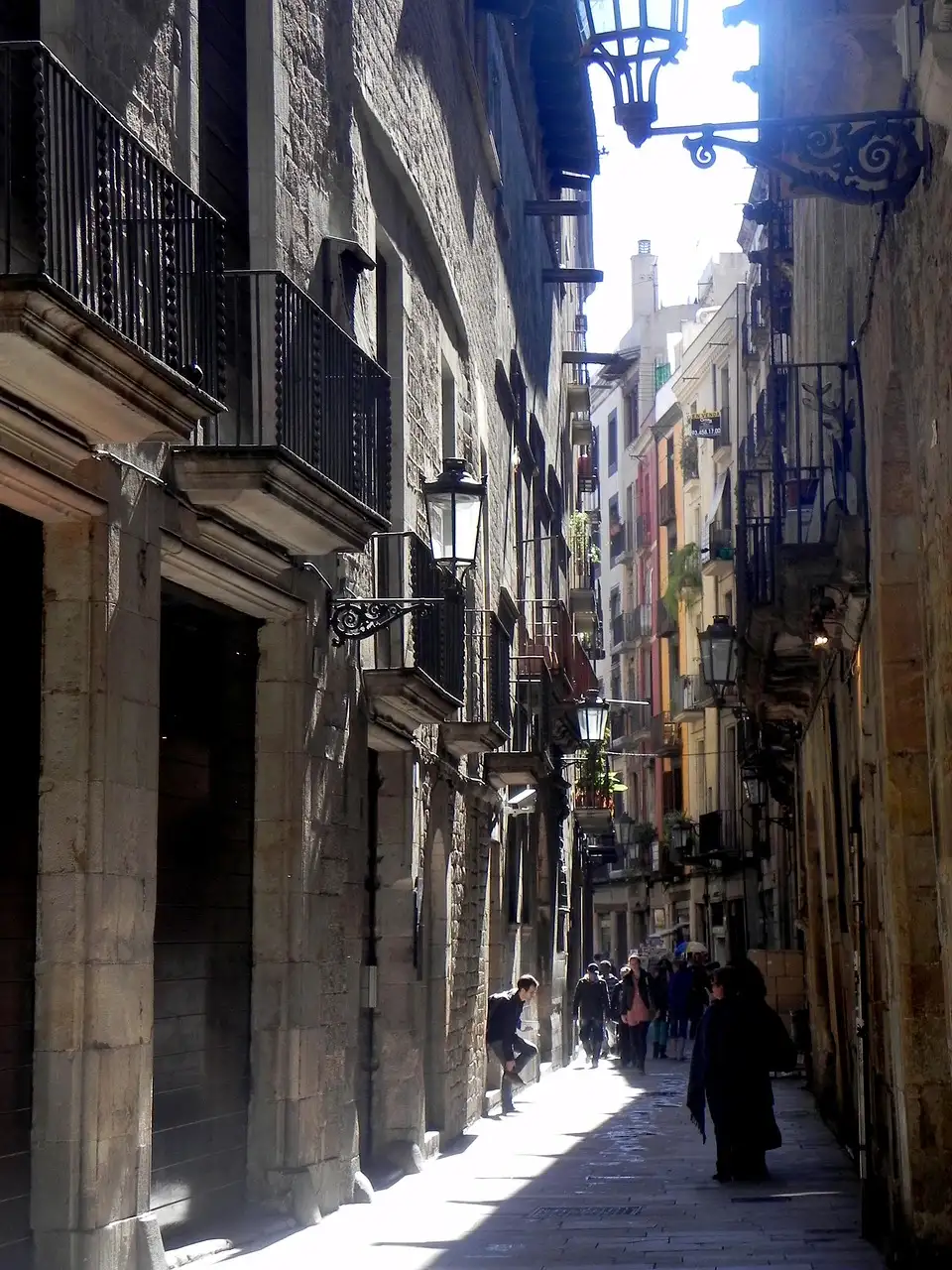 A sunny narrow street in Barcelona's Gothic Quarter lined with iron balconies and lamps