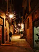 A narrow old-town lane at night, lit by wall lamps