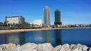 Calm sea and a sandy beach on Barcelona's seafront, with two tall towers behind