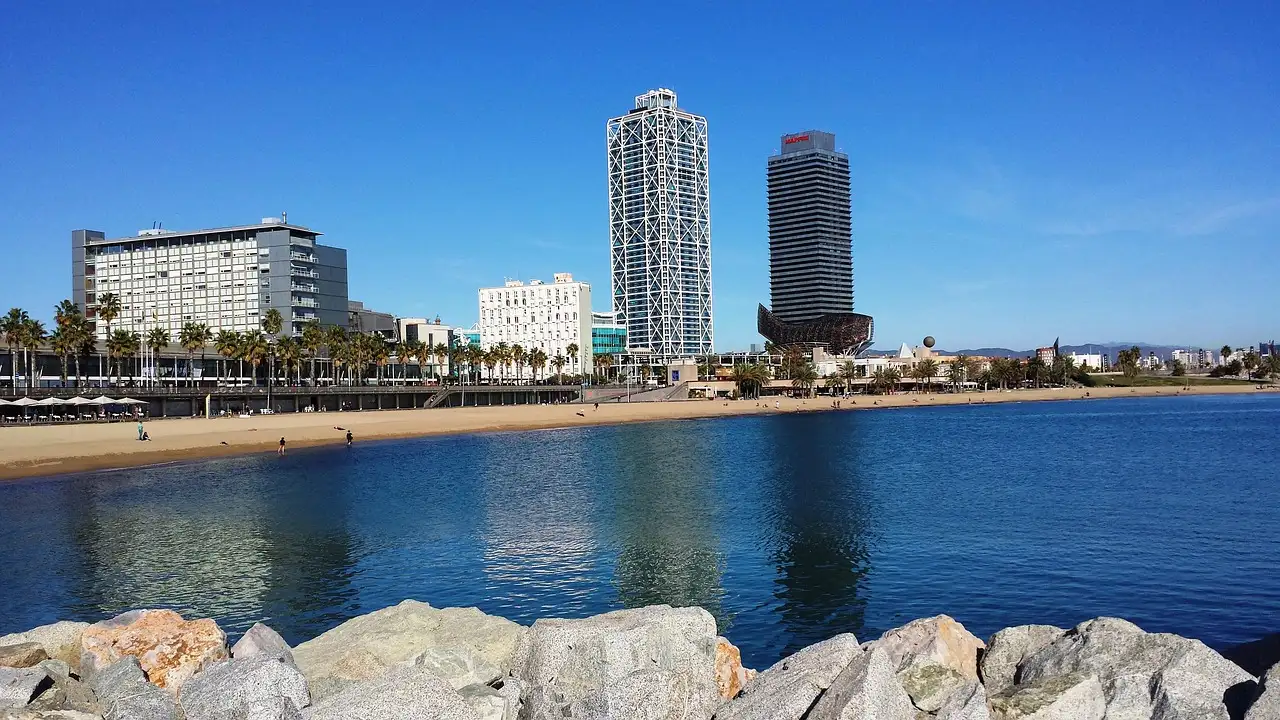 Calm sea and a sandy beach on Barcelona's seafront, with two tall towers behind