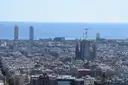 Barcelona's rooftops from a hill, with the Sagrada Família, two seafront towers and the sea behind