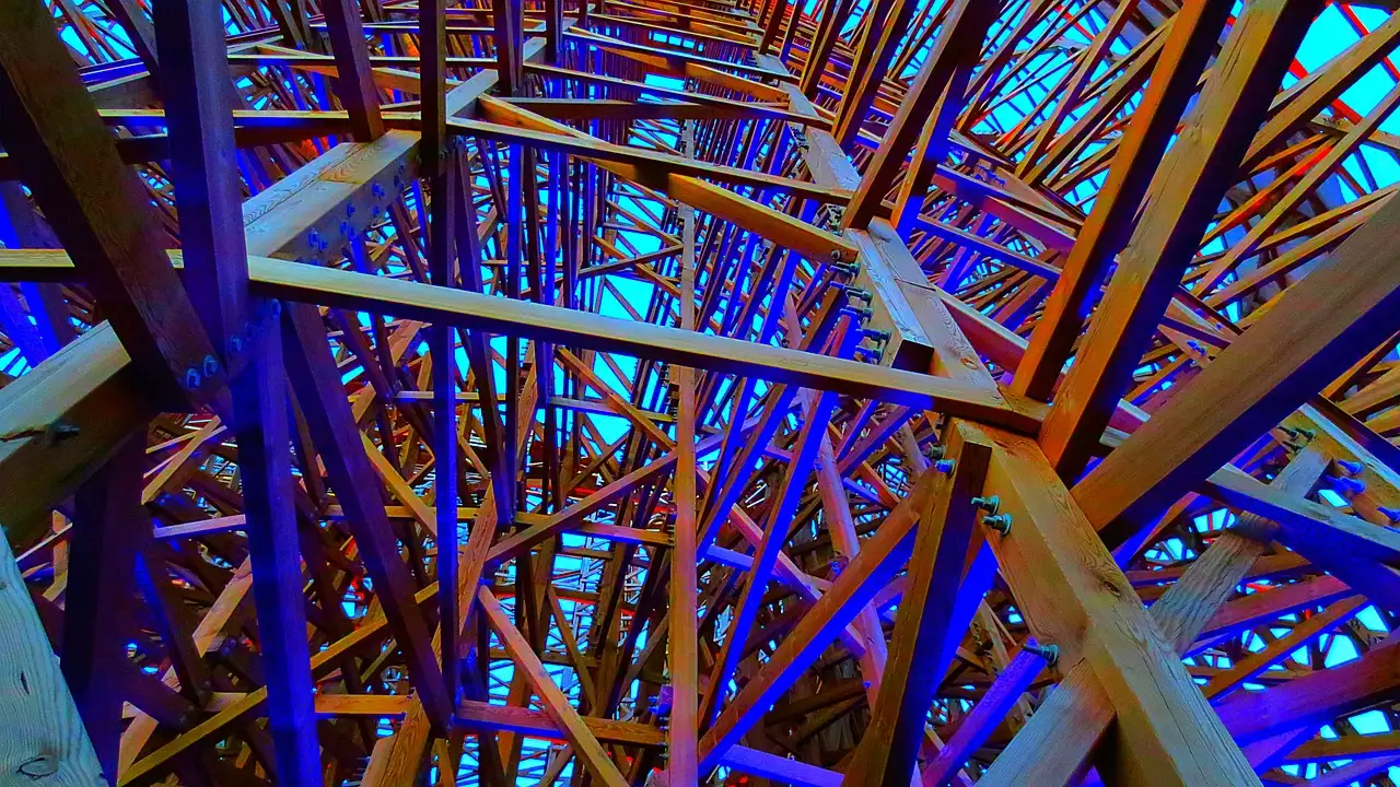 The wooden frame of a roller coaster lit in blue and purple