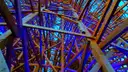 The wooden frame of a roller coaster lit in blue and purple